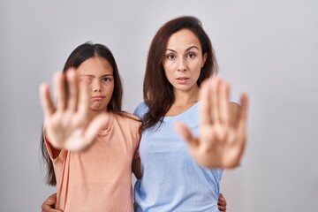 Young mother and daughter standing over white background doing stop sing with palm of the hand. warning expression with negative and serious gesture on the face.