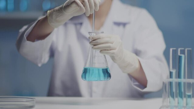A scientific researcher is gently stirring the light blue liquid in a erlenmeyer flasks with a glass rod. Science and medical background, skincare products and drugs chemical researches concept