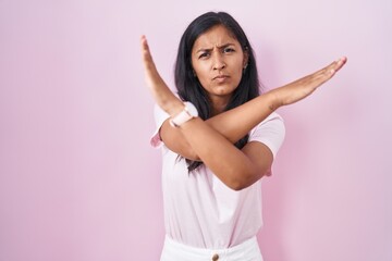 Young hispanic woman standing over pink background rejection expression crossing arms doing negative sign, angry face