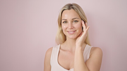 Obraz premium Young blonde woman smiling confident touching face over isolated pink background