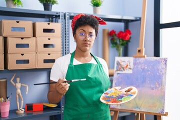 Young african american woman drawing on canvas at art studio skeptic and nervous, frowning upset...