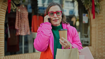 Mature hispanic woman with grey hair smiling going shopping speaking on the phone at clothing store