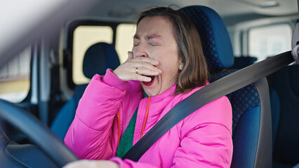 Mature hispanic woman with grey hair driving car yawning at street