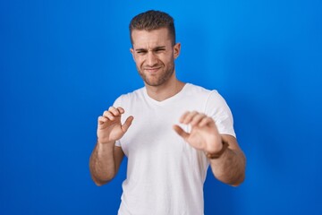 Naklejka premium Young caucasian man standing over blue background disgusted expression, displeased and fearful doing disgust face because aversion reaction.