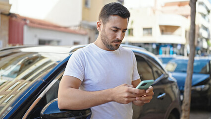 Fototapeta na wymiar Young hispanic man using smartphone leaning on car at street