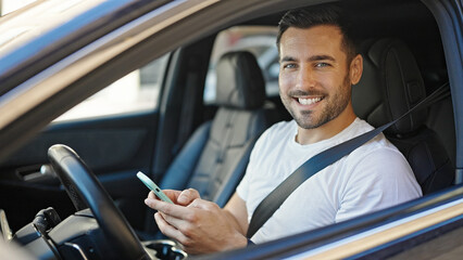 Young hispanic man using smartphone sitting on car at street