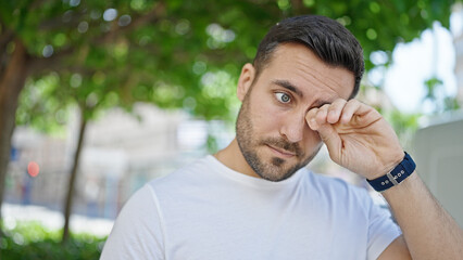 Young hispanic man standing with serious expression rubbing eyes at street