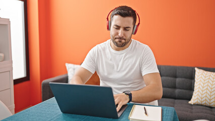 Young hispanic man listening to music sitting on table at dinning room