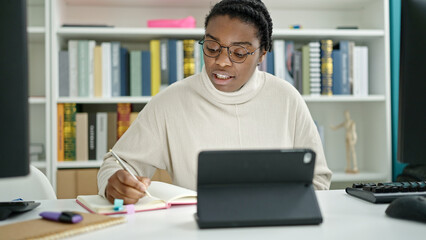 African american woman student using touchpad writing notes at library university
