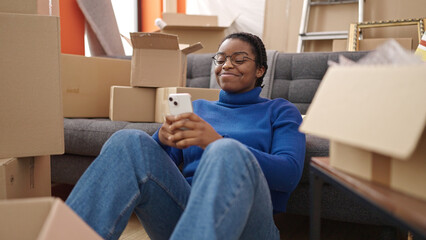 African american woman using smartphone sitting on floor at new home
