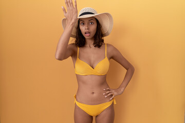 Young hispanic woman wearing bikini and summer hat surprised with hand on head for mistake, remember error. forgot, bad memory concept.