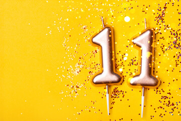 Gold candles in the form of number eleven on yellow background with confetti. 11 years celebration.