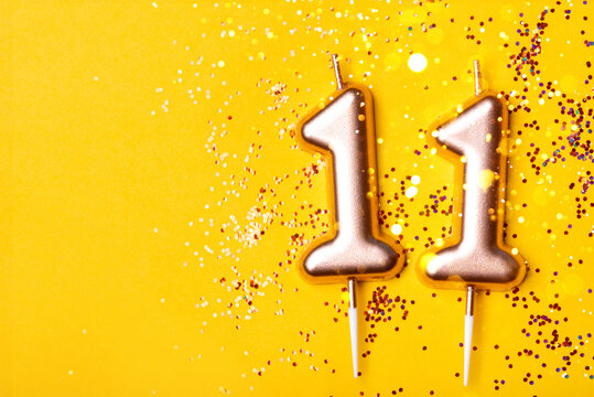Gold candles in the form of number eleven on yellow background with confetti. 11 years celebration.