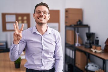 Young hispanic man at the office showing and pointing up with fingers number three while smiling confident and happy.