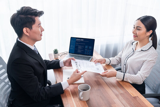 Conversational job interview between interviewer and candidate. Asian female job applicant present her performance and qualification by digital resume on laptop and CV paper to HR manager. Jubilant