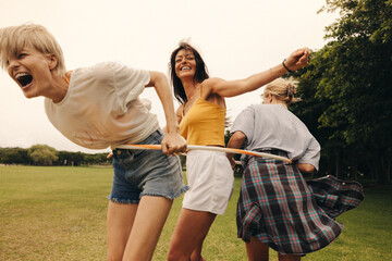 Female best friends laugh and have fun while playing with hula hoops in a park