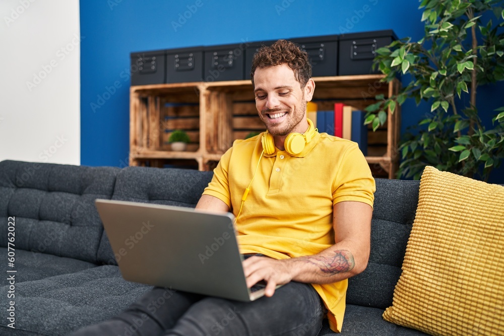 Sticker young hispanic man using laptop sitting on sofa at home