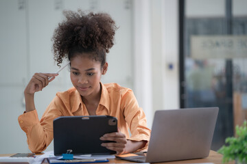 Focused young African female entrepreneur deep in thought while working at a table in a modern office.