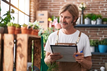 Young blond man florist smiling confident reading document at flower shop