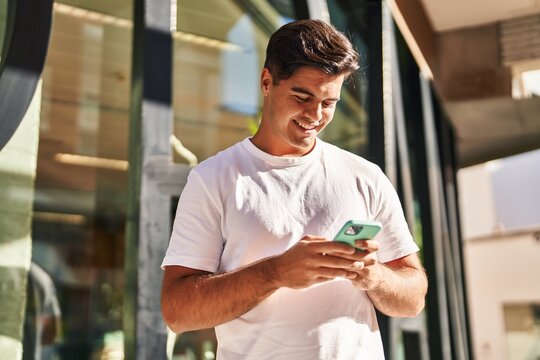 Young hispanic man smiling confident using smartphone at street