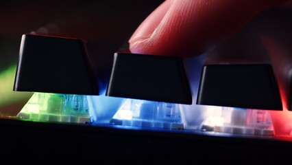 Human finger is on the keys on the computer keyboard, close up view. Finger  on the gaming keyboard key with led light, macro shot. Low angle view with a soft focus.