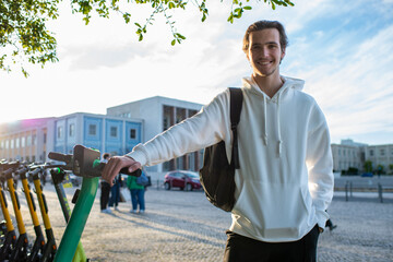 Student smiling while holding onto an electric scooter. Happy man standing close to an...