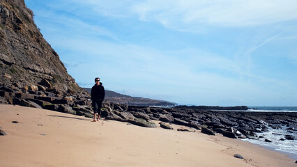 Man with a romantic mood relaxes on the beach contemplating the beautiful nature. Barefoot young man walks on the empty sandy beach on the summer day. Guy is walking on sandy beach on a sunny day.