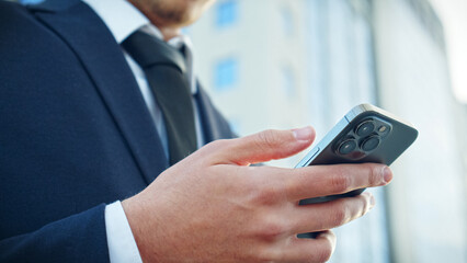 Businessman is typing text messages on mobile phone sitting in the park. Close up Male hands with...