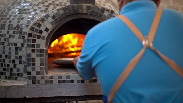 Slow motion of a chef cook placing a classic pepperoni pizza inside a traditional stone oven with wood burning and fire flames
