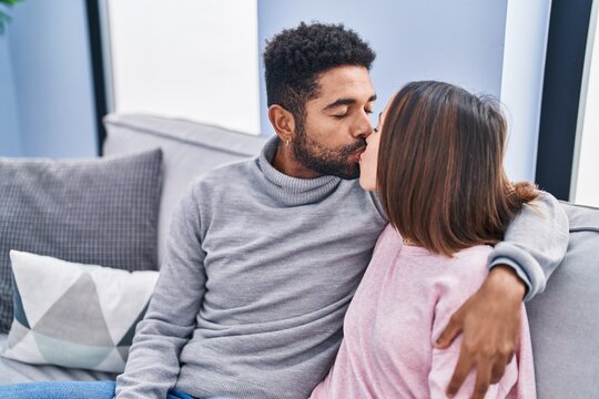 Man and woman couple kissing and hugging each other sitting on sofa at home