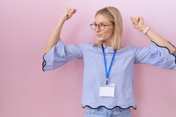 Young caucasian business woman wearing id card showing arms muscles smiling proud. fitness concept.