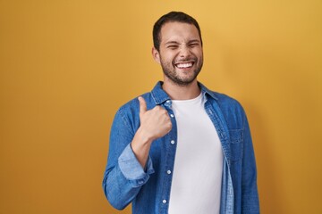 Hispanic man standing over yellow background doing happy thumbs up gesture with hand. approving expression looking at the camera showing success.