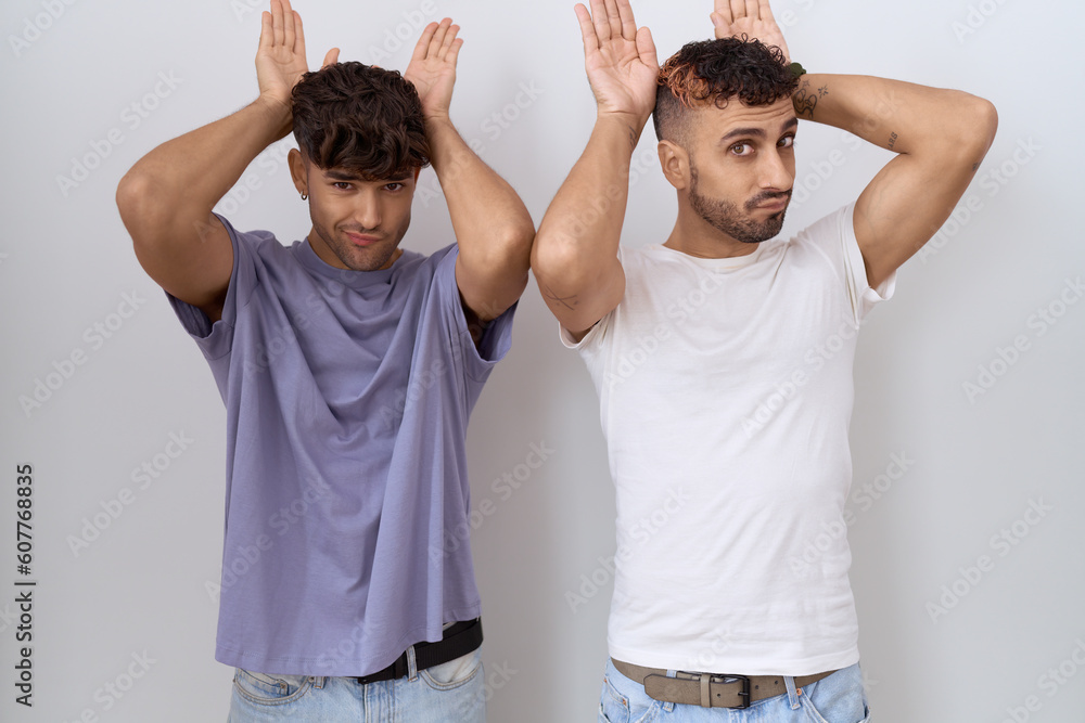 Poster homosexual gay couple standing over white background doing bunny ears gesture with hands palms looki