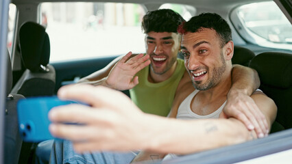Two men couple having video call sitting on taxi at street