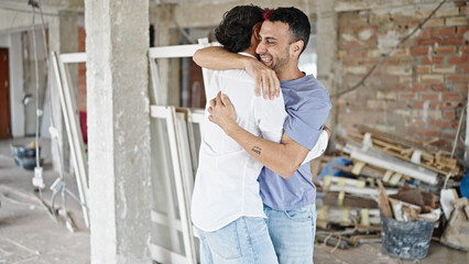 Two men couple smiling confident hugging each other at construction site