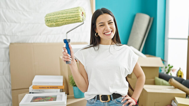 Young beautiful hispanic woman smiling confident holding paint roller at new home
