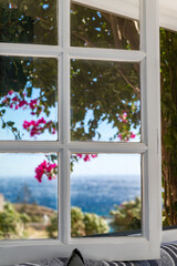 Window with Bougainvillea flowers tree and the Aegean Sea in Greece near traditional Cycladic houses