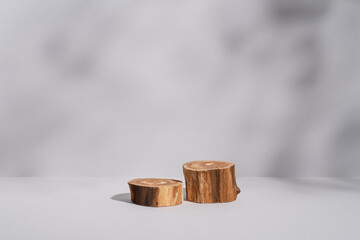 Two empty round wooden podium with leaf shadows on light grey background. Showcase or pedestal for beauty product presentation. Natural materials mockup. Eco concept. Copy space, front view.