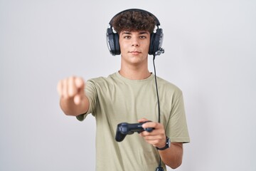 Hispanic teenager playing video game holding controller pointing to you and the camera with fingers, smiling positive and cheerful