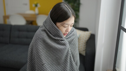 Young chinese woman covering with blanket for cold sitting on sofa at home