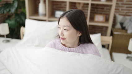 Young chinese woman smiling confident sitting on bed at bedroom
