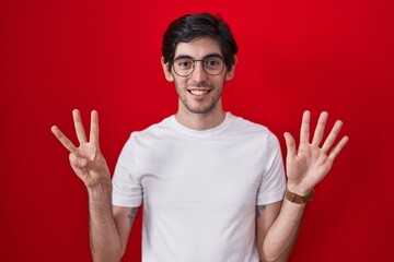 Naklejka premium Young hispanic man standing over red background showing and pointing up with fingers number eight while smiling confident and happy.