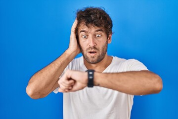 Hispanic young man standing over blue background looking at the watch time worried, afraid of getting late