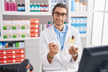 Young hispanic man pharmacist smiling confident holding pills bottles at pharmacy