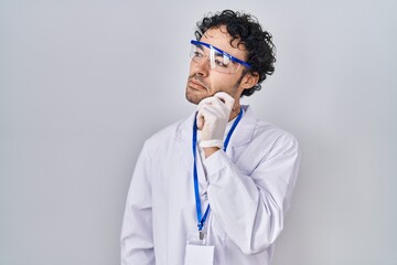 Hispanic man working at scientist laboratory thinking concentrated about doubt with finger on chin and looking up wondering