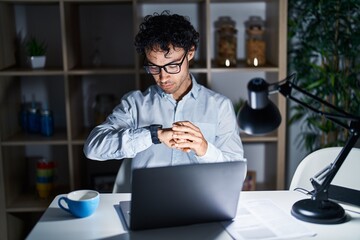 Hispanic man working at the office at night checking the time on wrist watch, relaxed and confident