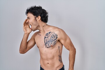 Naklejka premium Hispanic man standing shirtless shouting and screaming loud to side with hand on mouth. communication concept.