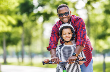 Happy family father teaches child  son  to ride bike in park