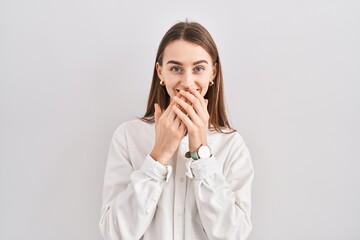 Young caucasian woman standing over isolated background laughing and embarrassed giggle covering...