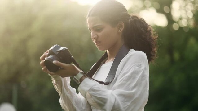 Portrait of sad young indian woman photographer dissatisfied her photos at camera and expressively delete it outdoors Lack of inspiration and creative crisis concept